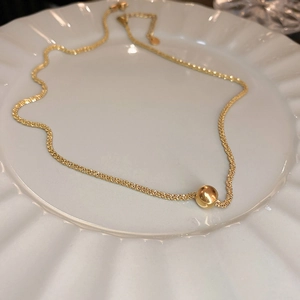 Detailed shot of a gold ball pendant necklace on a decorative white ceramic plate