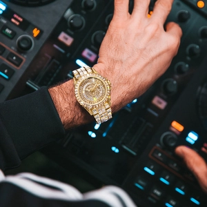 Luxury men's gold watch with full diamond setting on a DJ mixer background