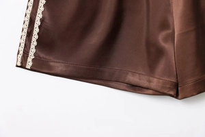 Detail of dark brown satin shorts featuring delicate white lace trim on the hemline