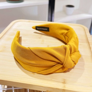 Detail of yellow fabric headband with cross-knot design and handmade label on bamboo tray