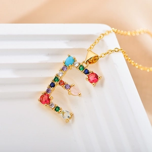 Elegant gold letter F necklace with colorful cubic zirconia on a white pedestal