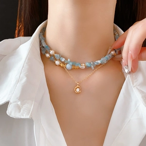 Detail of layered gold necklace with blue aquamarine stones and a pearl ring pendant