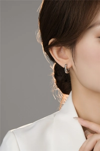 Close-up of minimalist silver hoop earring with irregular texture worn on ear