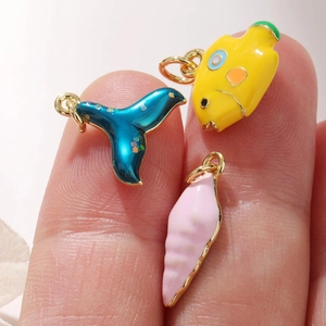 Detail of whale tail, fish and conch enamel charms held by hand showing compact size