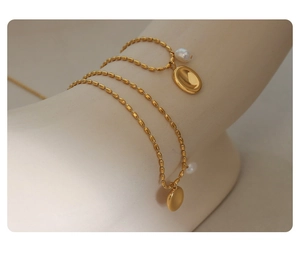 Detail of gold oval pendant and freshwater pearl on a thin beaded chain necklace