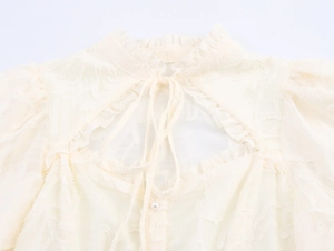 Detail of ruffle stand collar with cutout design, ribbon tie and pearl button blouse