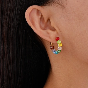 Close-up of a colorful rainbow crystal beaded C-shaped hoop earring on a model ear