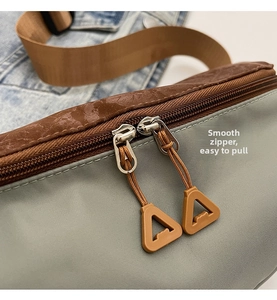 Detail of smooth two-way zippers with brown woven pulls on green nylon crossbody bag