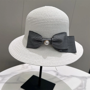 Detailed view of a white straw sun hat featuring a black plaid bow and pearl accent