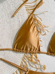 Close-up of golden satin triangle bikini top with glossy fabric on woven beach mat