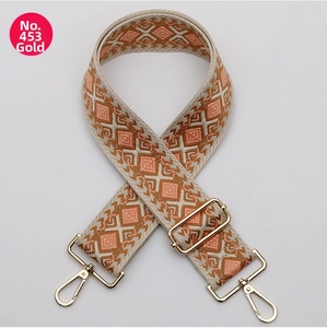 Detail of embroidered geometric bag strap with orange diamond patterns and gold hooks