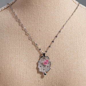 Elegant silver pendant necklace with pink teardrop gemstone on a linen display stand