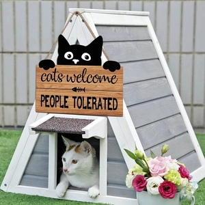 Wooden cat welcome sign hanging on a white cat house with a cat peeking out