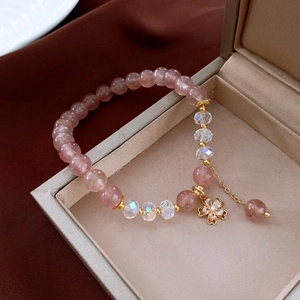 Close-up of pink crystal bead bracelet with gold clover pendant on brown silk fabric