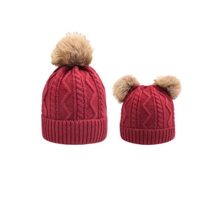 Detail of burgundy cable knit parent-child hat set with fluffy faux fur pom poms
