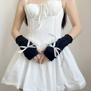 Detail of black knitted arm sleeves with white ribbon bows worn over a white dress