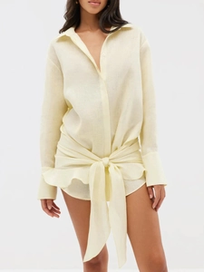 Detail of light yellow shirt dress featuring waist tie and elegant ruffle hemline