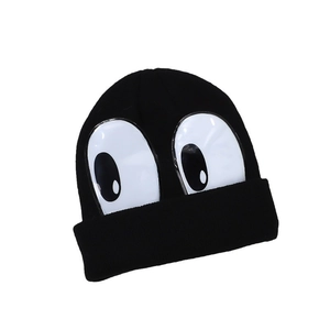 Cute black knit beanie for kids with large white cartoon eyes decoration on plain background