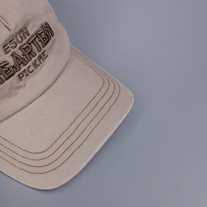 Close-up of beige baseball cap featuring brown embroidery and fine parallel stitching