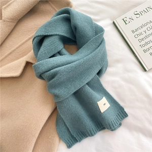 Detail of teal knitted scarf with ribbed edges and small emo label on white fabric