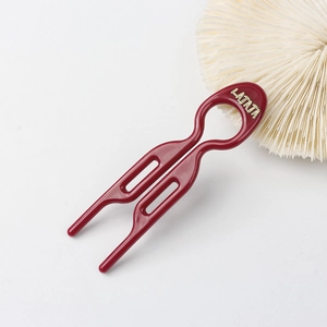 Detail of dark red resin hair fork with two prongs and gold brand logo on white background