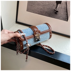 Detail of blue denim cylinder bag with brown leather trim and silver chain strap