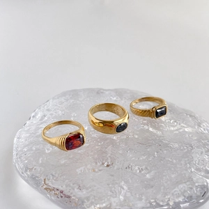 Detailed view of three gold rings with red and black gemstones on a glass tray