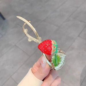 Close-up of strawberry hair clip with red enamel and gold-tone metal floral details