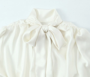 Close-up of elegant white satin shirt featuring a detailed bow-tie neckline and glossy fabric