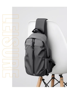 Detail of a dark gray water-resistant sling bag with multiple zippers hanging on a white chair