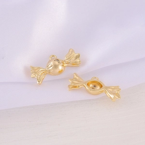 Two golden candy shaped metal pendants for DIY jewelry making on white silk background