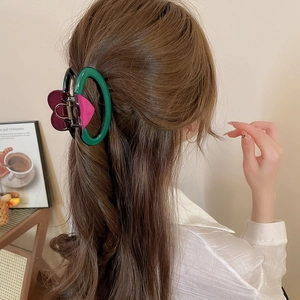 Détail d'une pince à cheveux en acrylique rouge et vert sur de longs cheveux bruns