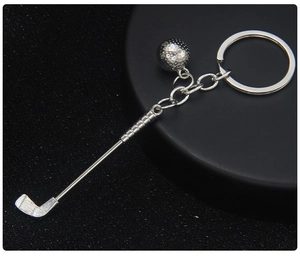 Close-up of a silver metal golf club and ball keychain on a dark matte circular base