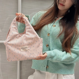 Floral canvas lunch bag in pink and blue held by a model in a green sweater
