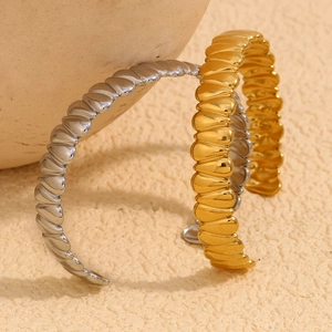 Polished 18K gold and silver plated wave-textured open cuff bracelets on ceramic base