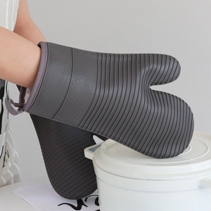 Heat resistant dark gray silicone oven mitts used to hold a white ceramic casserole pot