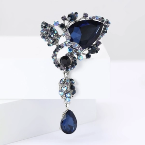 Elegant silver brooch with deep blue teardrop gems and purple rhinestones in floral design