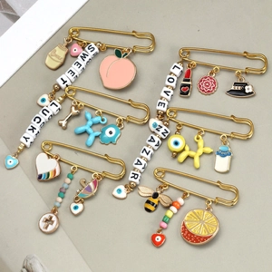 Detail of gold enamel pins with evil eye, balloon dog and heart charms on a grey surface