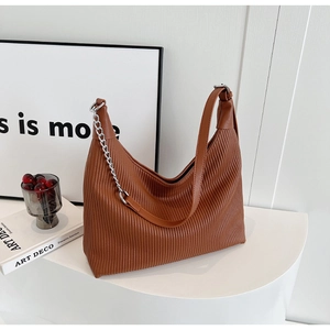Détail d'un sac cabas plissé marron avec chaîne argentée sur un support d'exposition