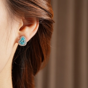 Close-up of blue pear-shaped zircon earring with crystal halo on a model's ear