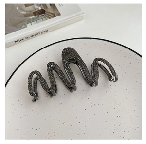 Close-up of grey shark hair claw clip with rhinestones on a decorative ceramic plate