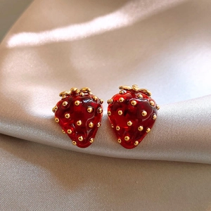 Pendientes de fresa lindos en rojo y dorado sobre elegante tela de seda brillante