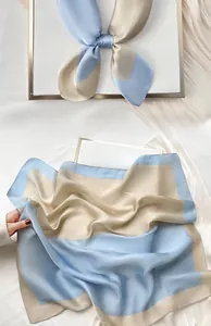 Detail of silk-like square scarf in light blue and beige color block on gold tray