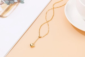 Detail shot of golden heart pendant necklace with adjustable bead on beige background