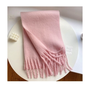 Flat lay of pink mohair scarf with tassels on a white table with candle and card