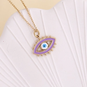Macro shot of gold evil eye necklace with purple enamel detail on white shell stand