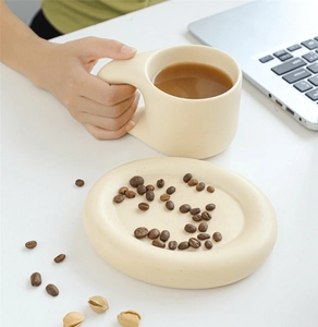 Detail of a beige ceramic mug with a chunky handle on a matching tray with coffee beans