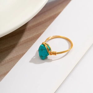 Detail of handmade gold wire-wrapped ring featuring irregular turquoise stone on white display