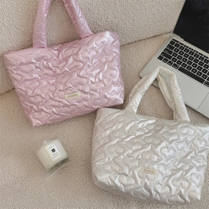 Detail of pink and white heart-quilted nylon handbags with glossy texture on soft rug
