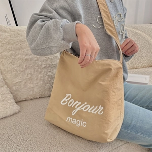 Dettaglio della borsa tote in tela beige con stampa Bonjour magic indossata da una modella